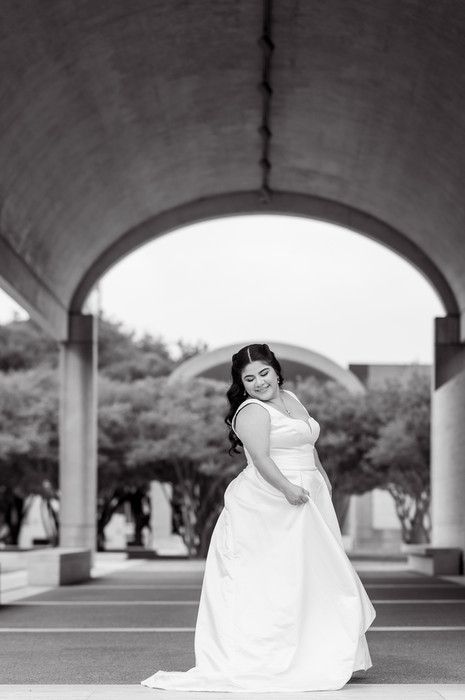 Bride in white gown twirling under arched concrete structure in elegant black and white bridal portrait.