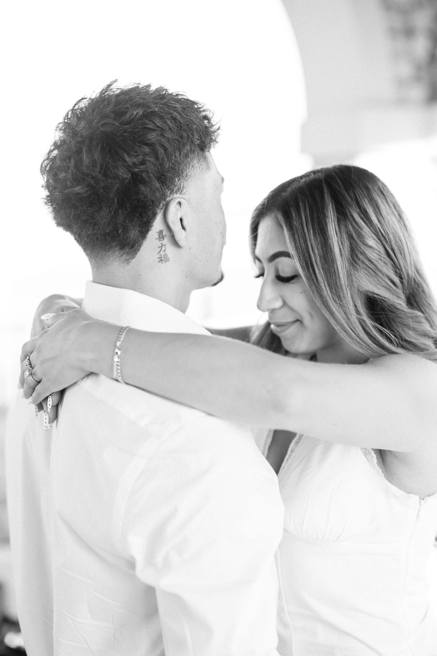 Black and white photo of a couple in white outfits sharing an intimate moment, woman resting her head near mans shoulder.