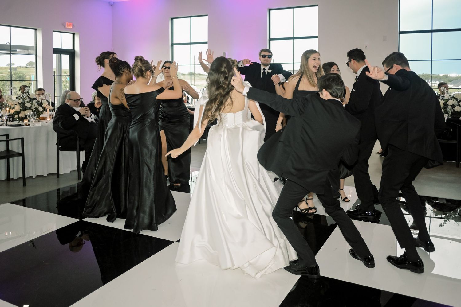Bride and wedding party dancing energetically on a black and white checkered dance floor at reception.