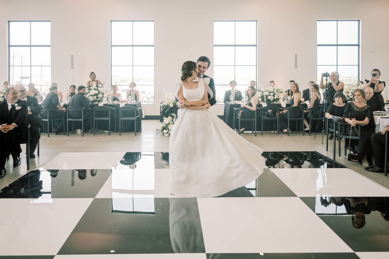 Bride and groom sharing first dance on black and white checkered dance floor at wedding reception.