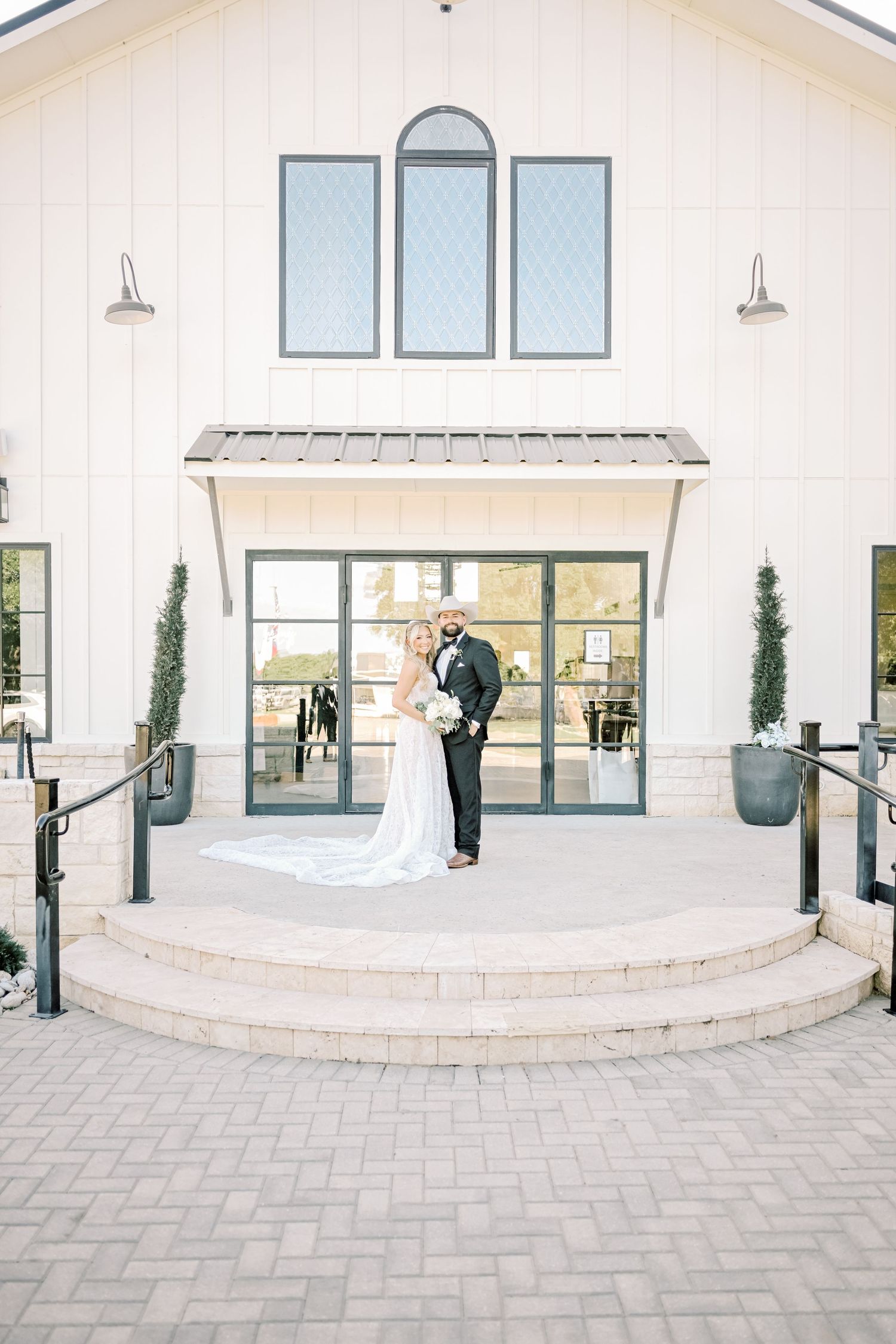 Bride and groom share a kiss on steps outside a white modern farmhouse wedding venue.