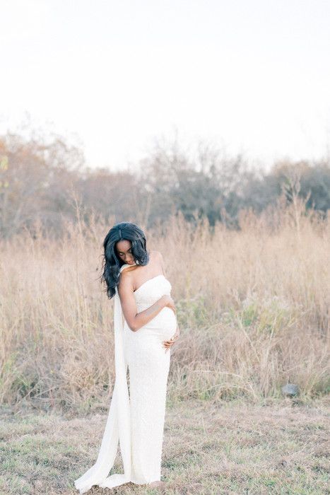 Two people in white outfits embrace lovingly in a sunlit field of tall grass during a romantic outdoor photoshoot.