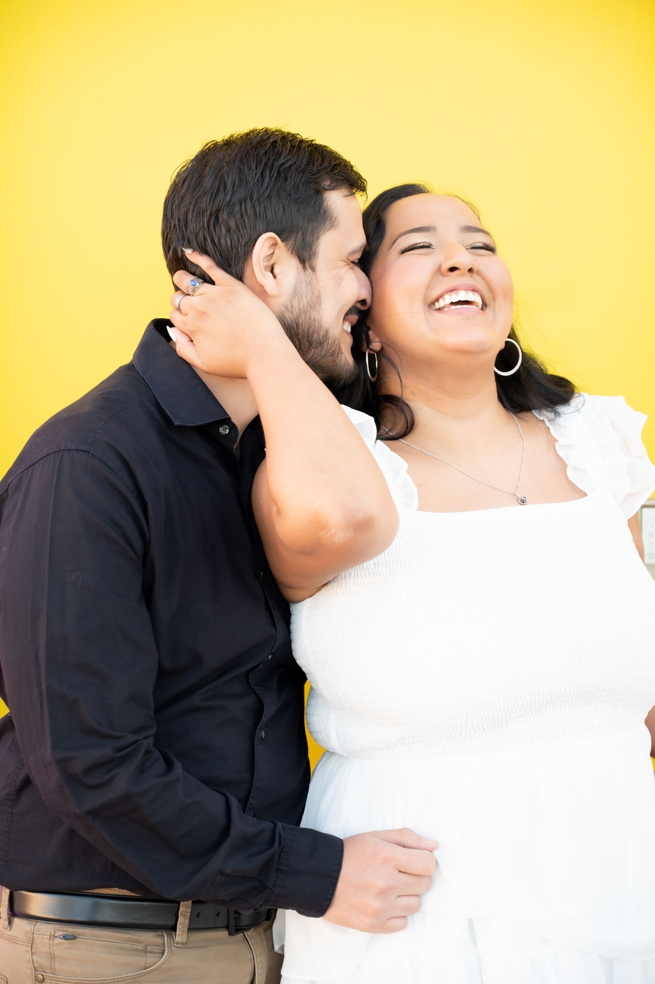 Joyful couple sharing laughter and tender moment against vibrant yellow backdrop.