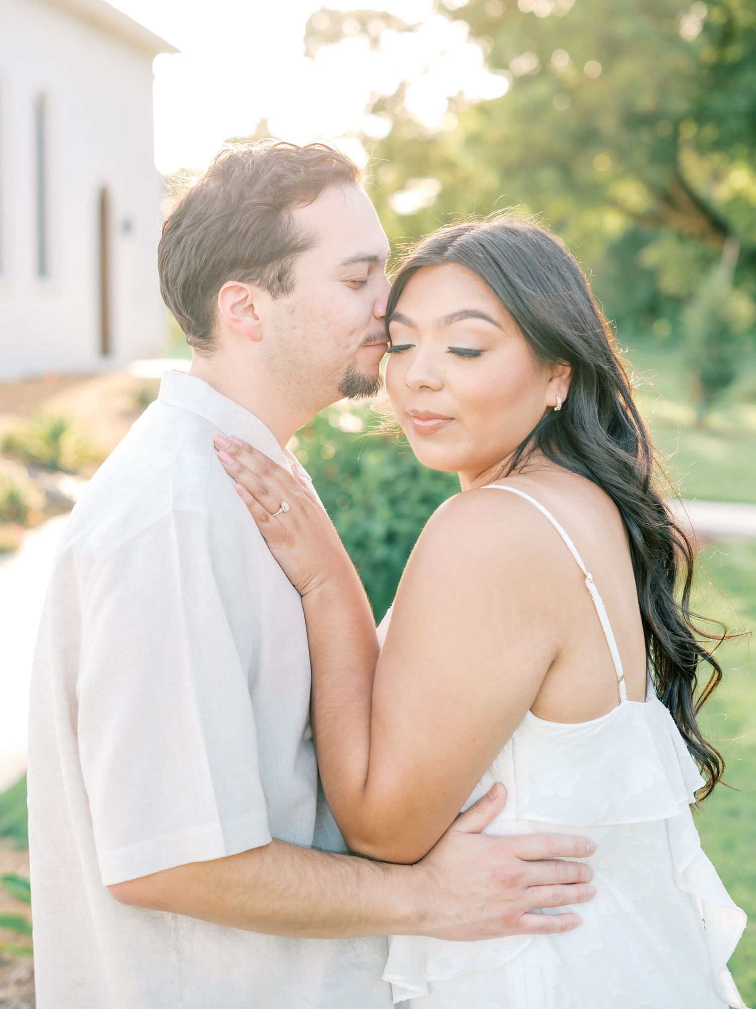 A romantic couple embraces outdoors during a sunset photoshoot in a garden setting.