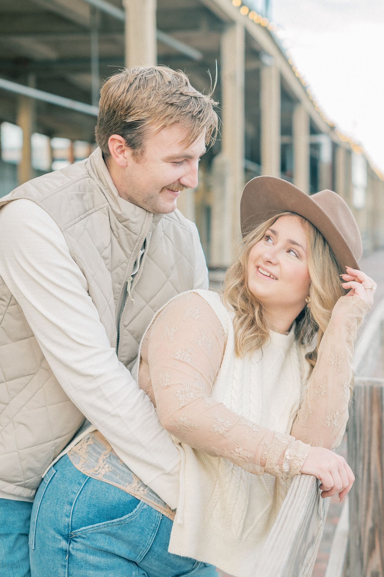 A couple in casual western attire share a romantic moment under a covered porch.