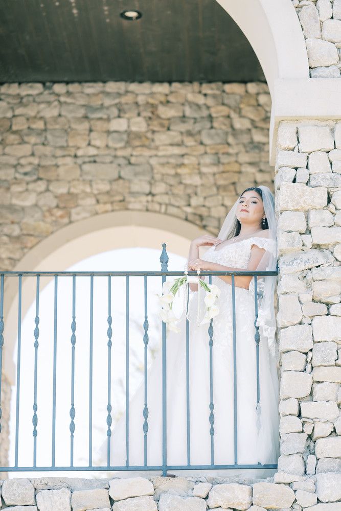 Dreamy bridal portrait in stone archway with blue metal railings and soft natural lighting.