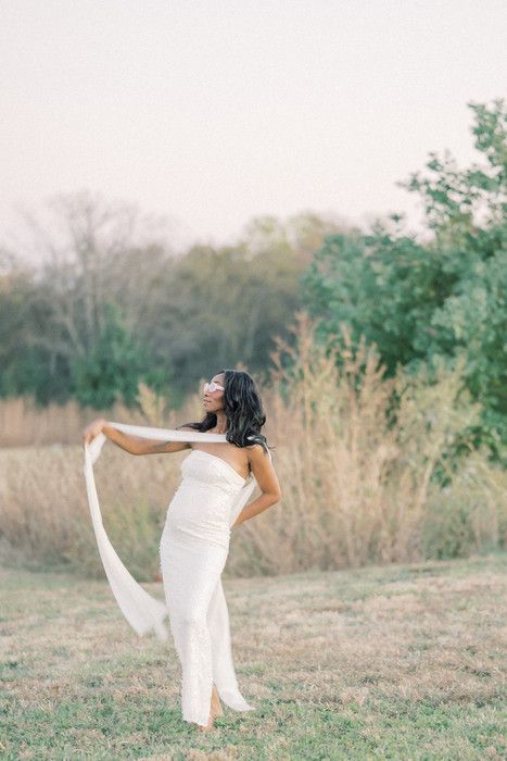 Dancing maternity portrait with flowing white dress in rustic outdoor setting.