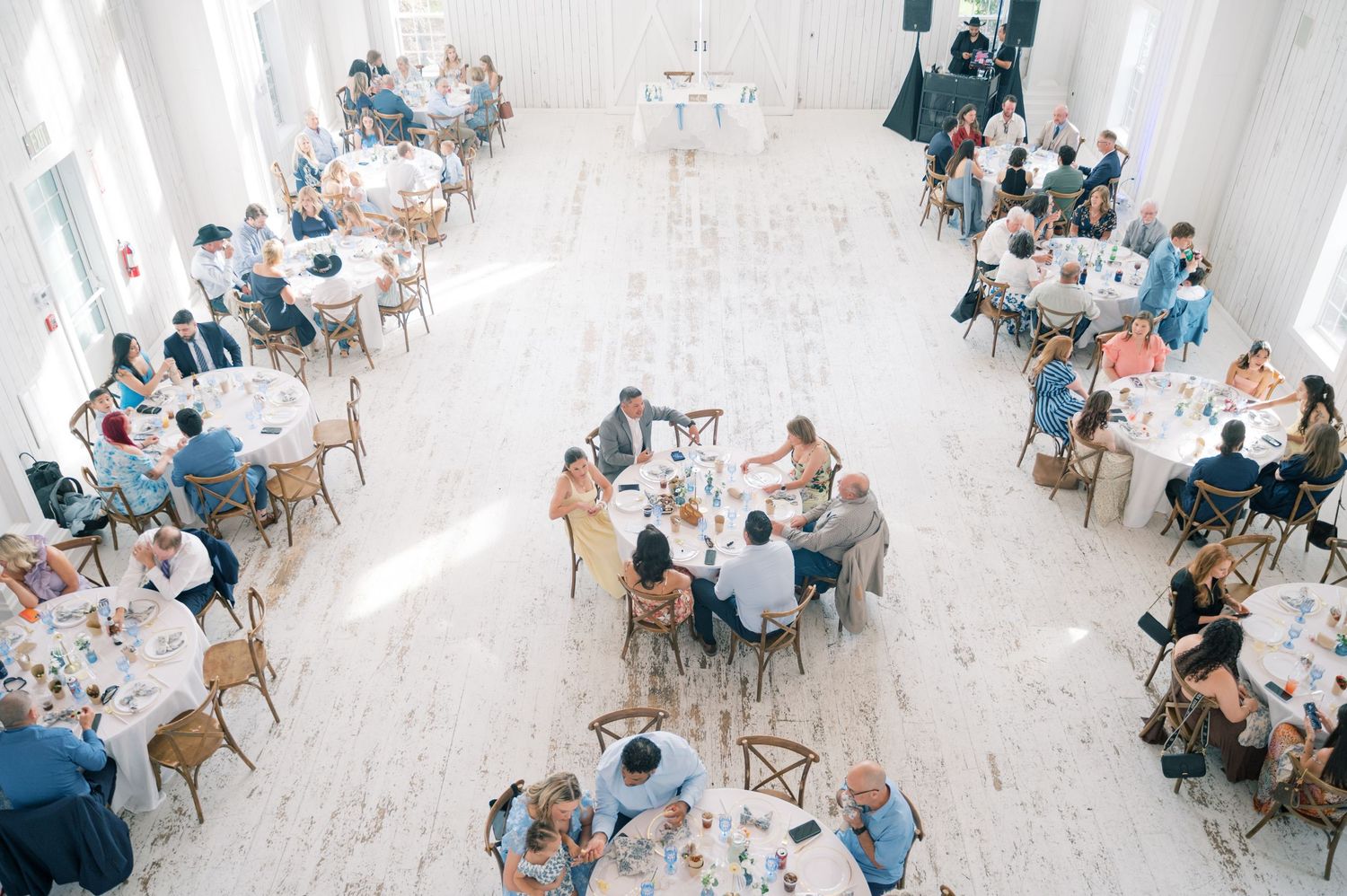 Aerial view of wedding reception guests seated at round tables in bright white event hall.