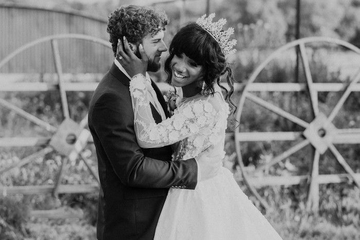 Black and white artistic wedding portrait against a rustic fence backdrop.