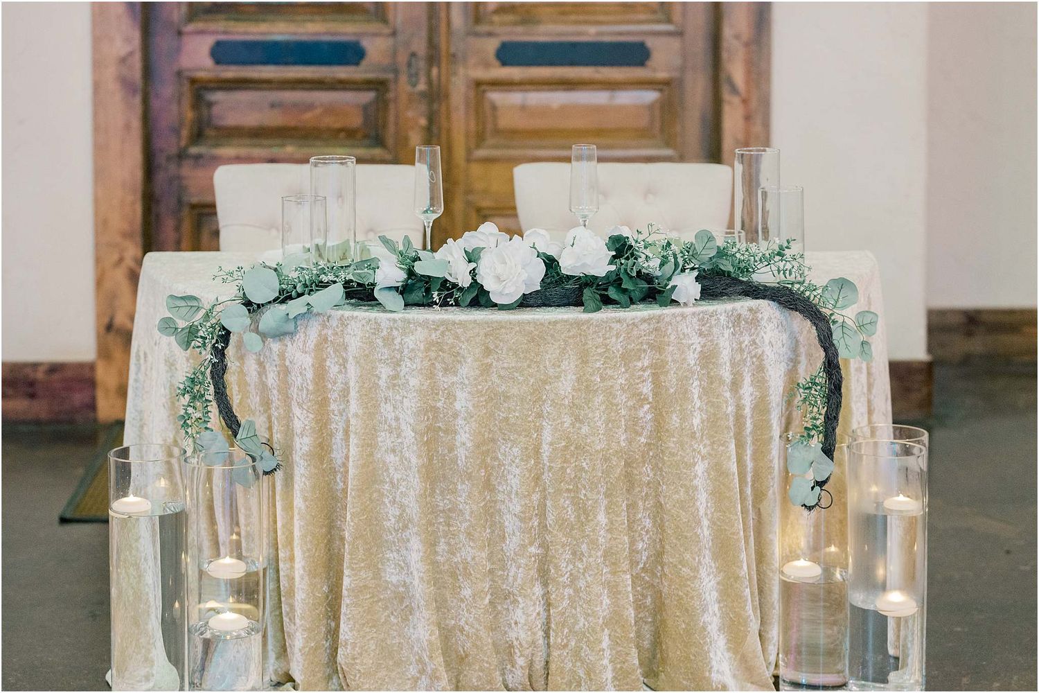 Elegant wedding reception tables decorated with sequined linens, greenery, and glowing candles create a romantic atmosphere.