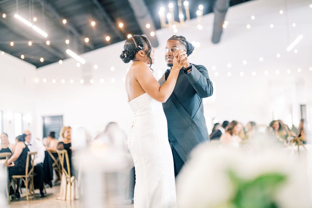 Bride and groom share their first dance at an elegant wedding reception with string lights overhead.