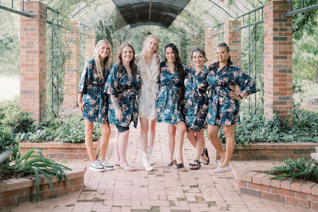 Six women in matching navy floral robes smiling together under a garden archway on a brick path.