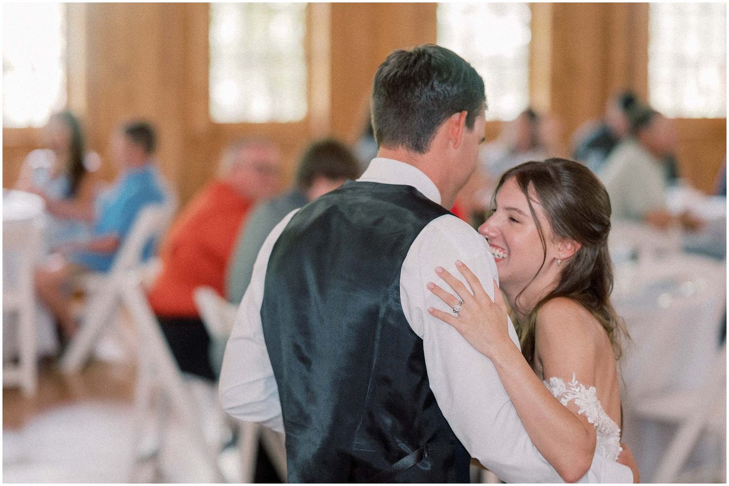 A romantic first dance between newlyweds at their wedding reception as guests look on in the background.