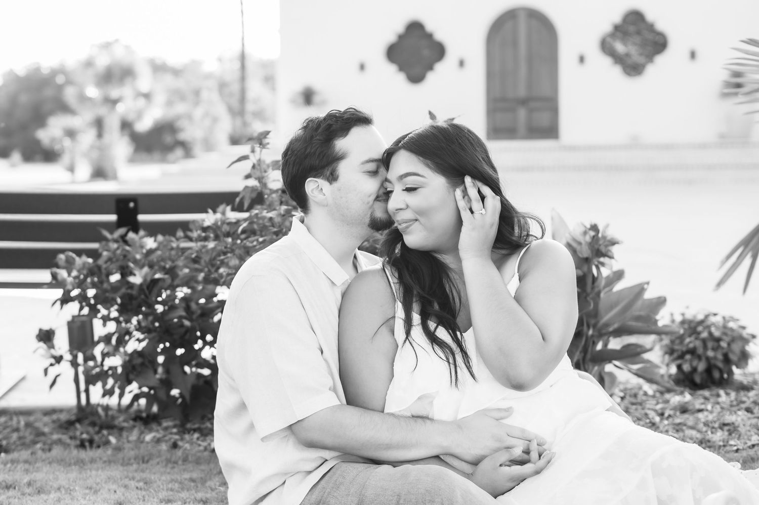 A couple shares an intimate moment in a lush garden with tropical plants and red flowers.