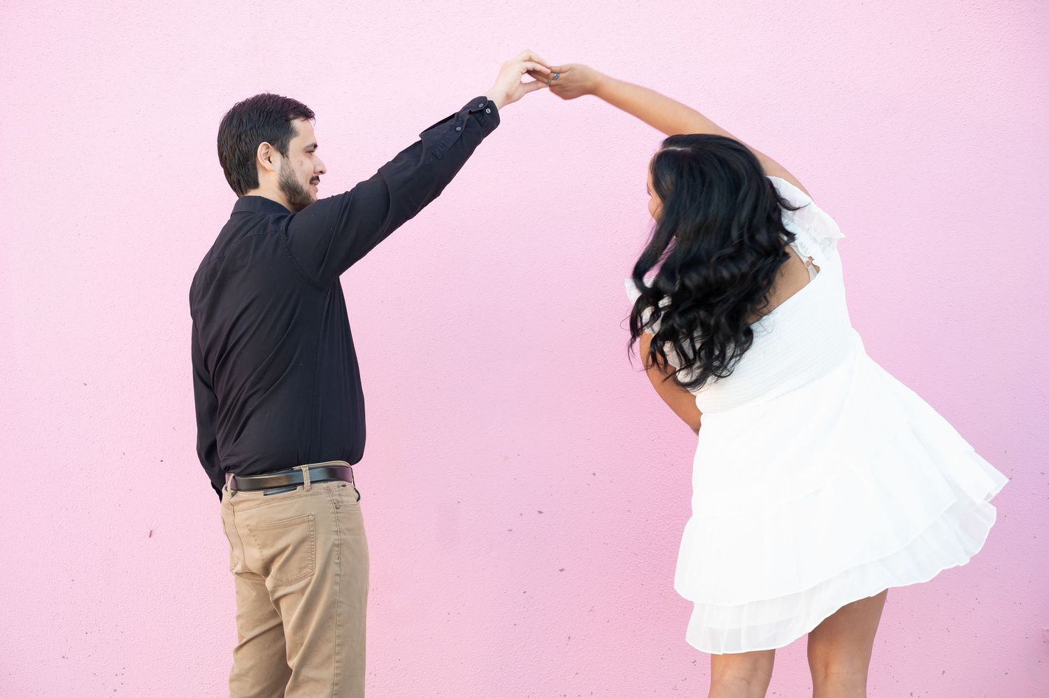 A couple executes a playful dance lift against a pink studio background.