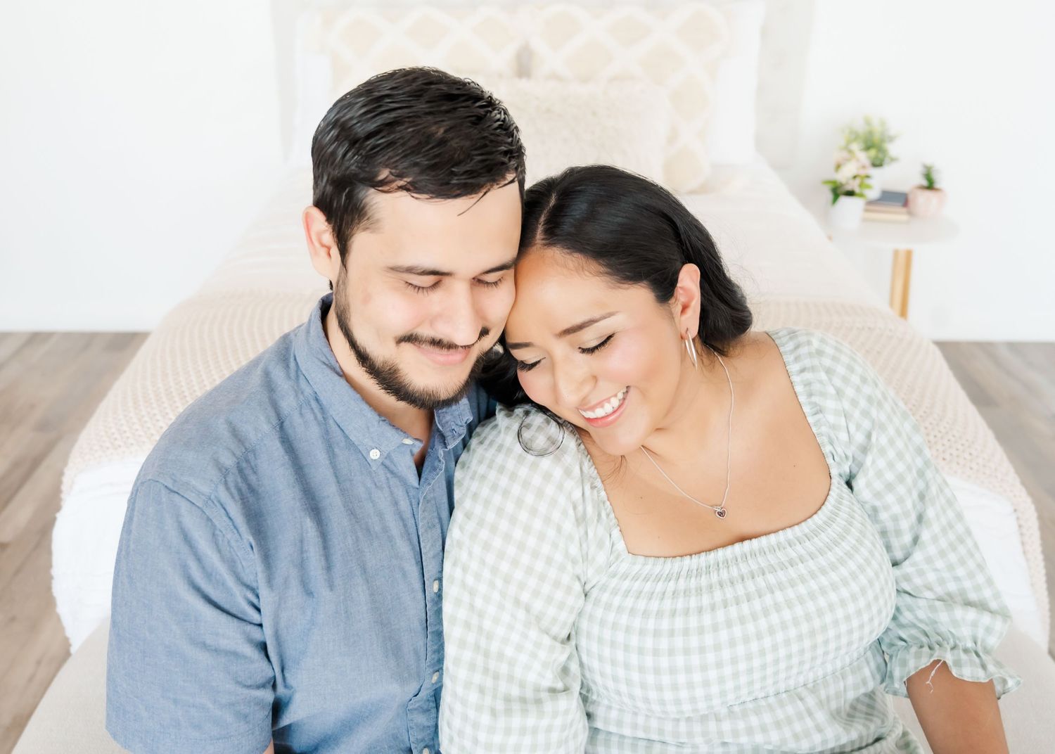 A couple leans in close together while sitting on a white couch in a bright room.