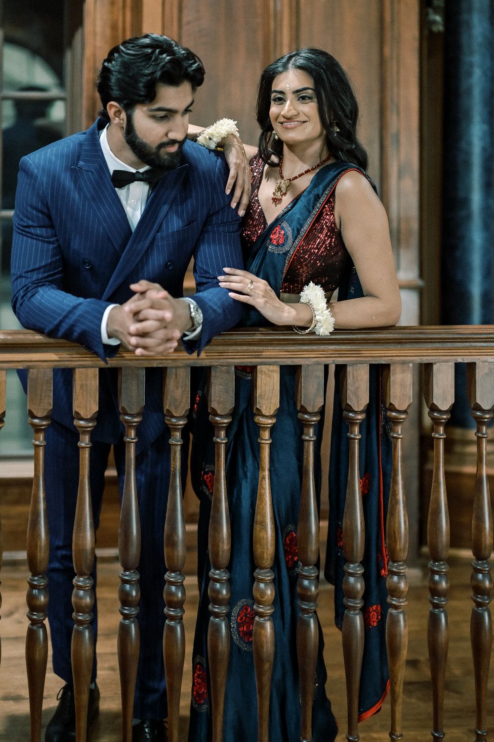 Couple in formal attire shares moment on wooden balcony with ornate details.