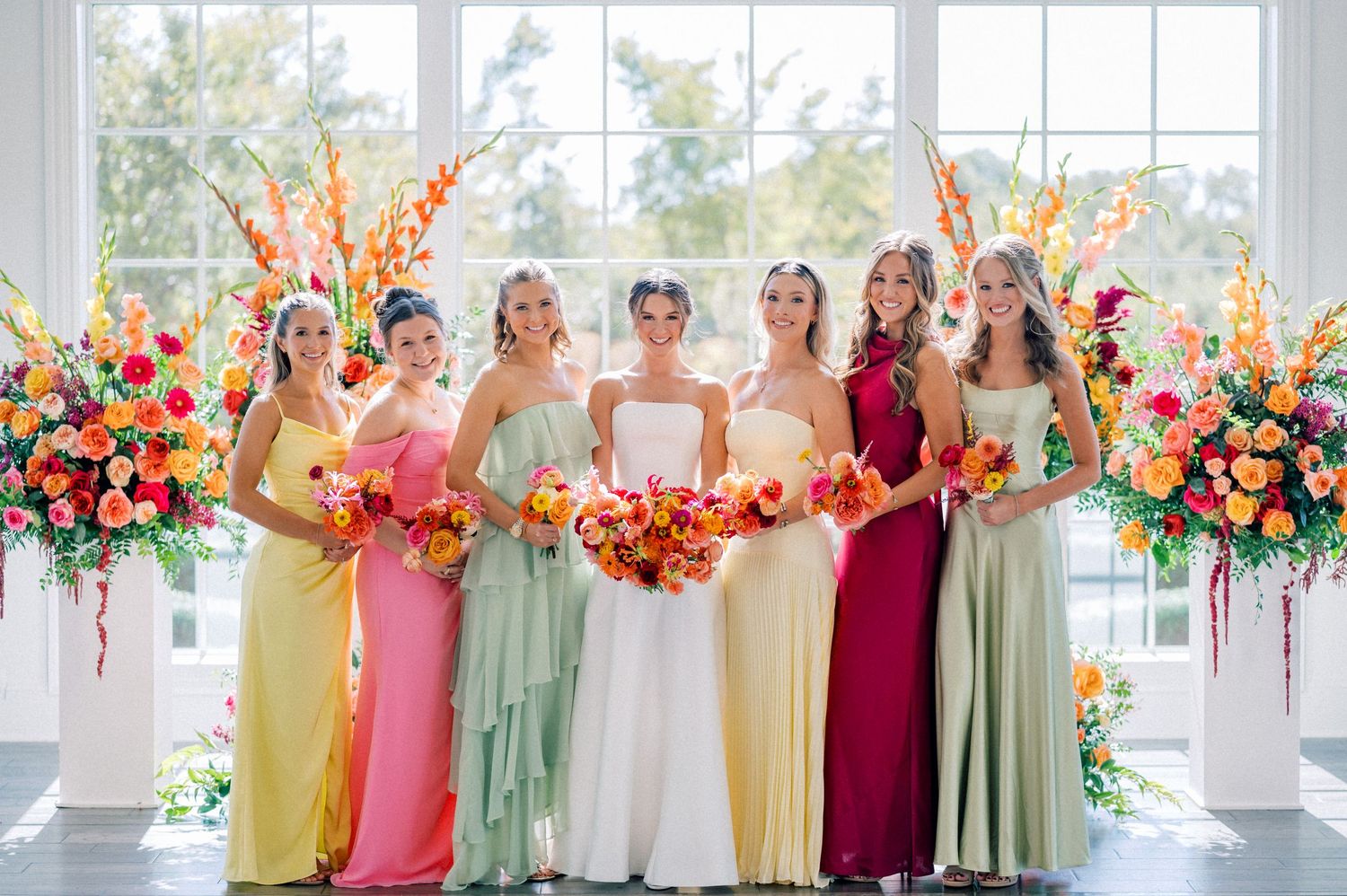 Wedding party lineup showing bridesmaids in multicolored dresses with bright floral arrangements.