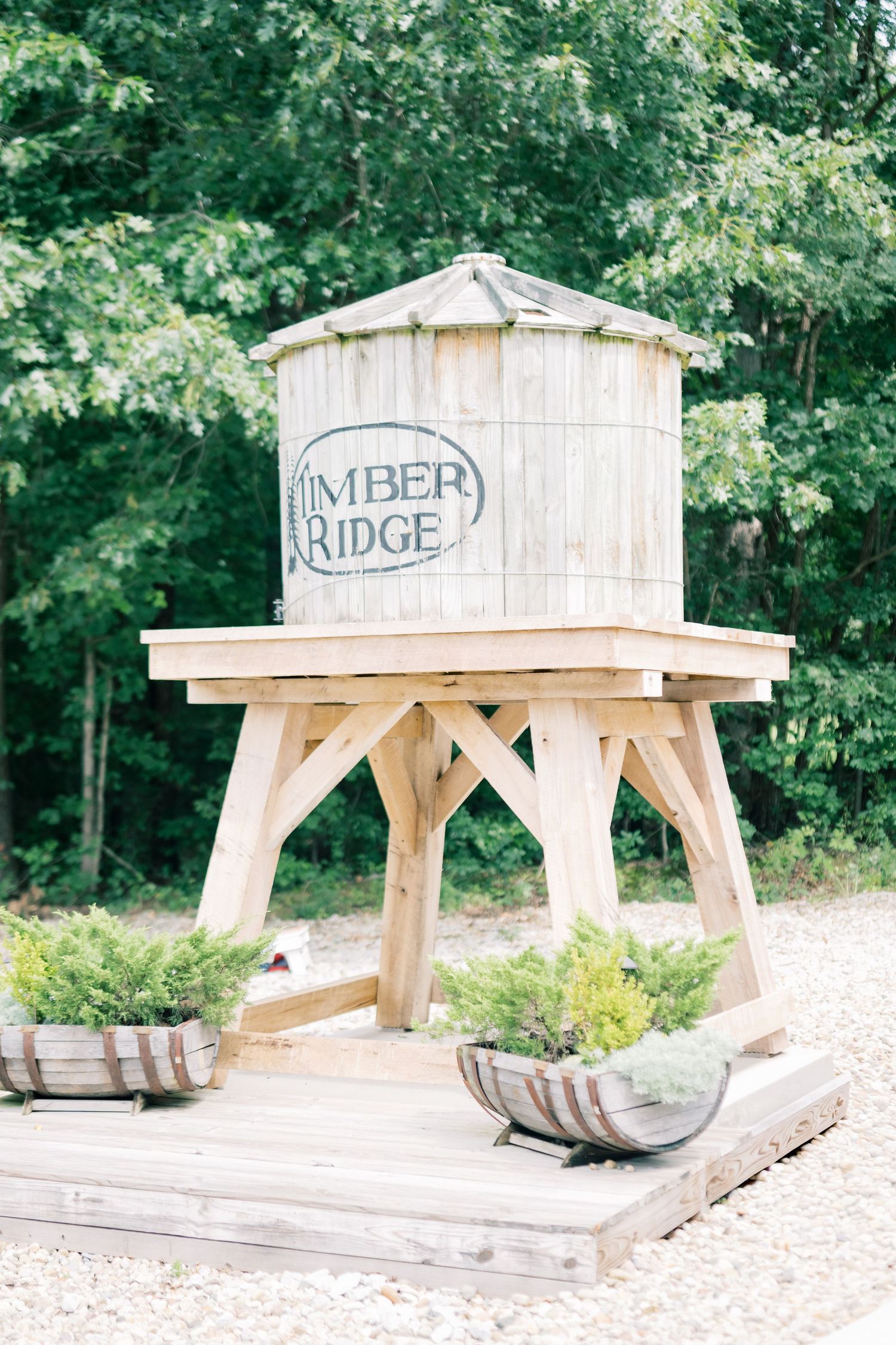 Rustic wooden water tower with Timber Ridge sign on a timber frame platform surrounded by greenery.