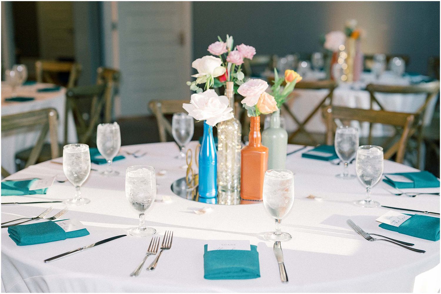 Wedding reception tables set with teal napkins and delicate floral centerpieces.