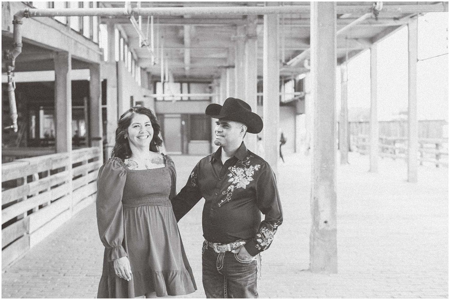 Couple poses together in bright industrial space with concrete columns and natural lighting.