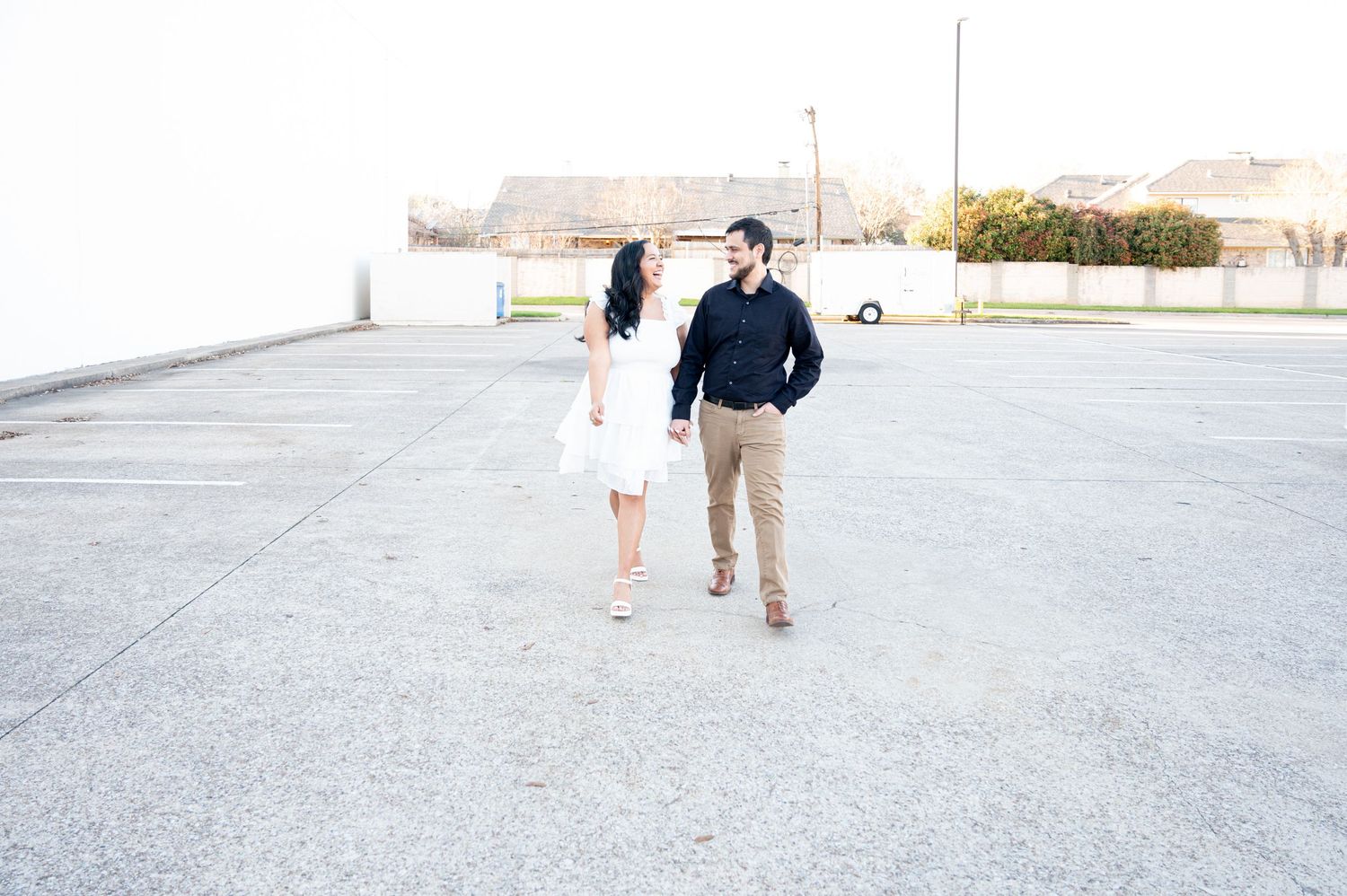 A couple walks together on a bright concrete surface while holding hands on a sunny day.