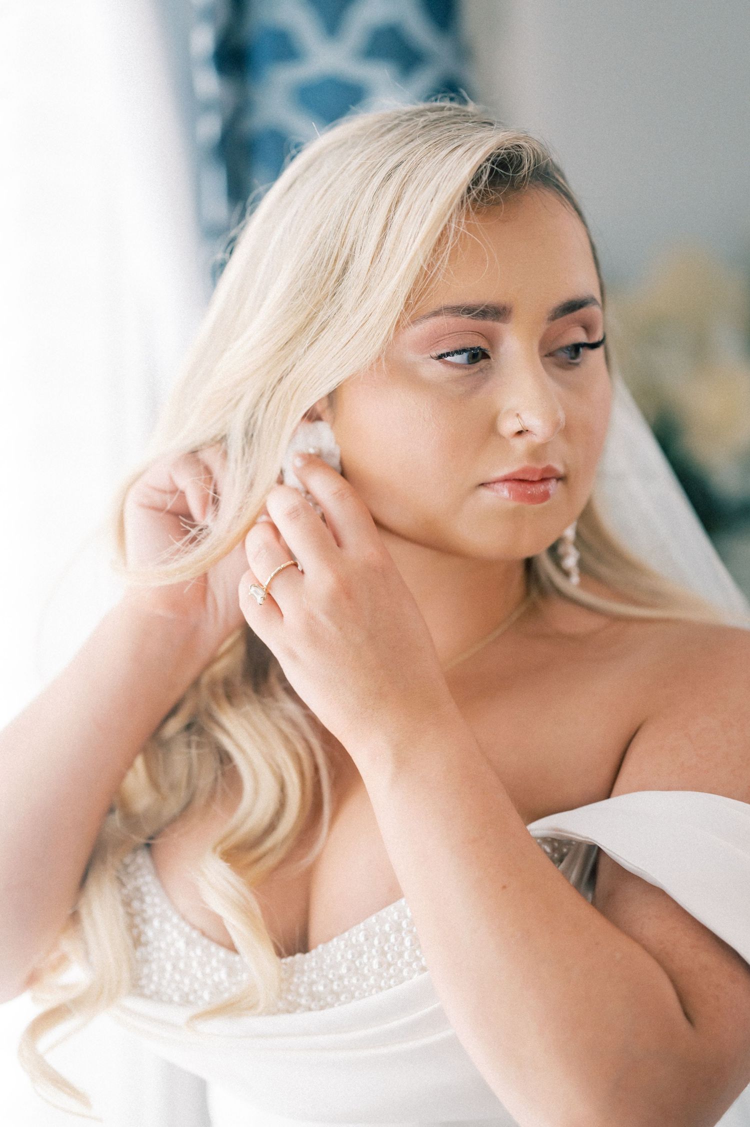 Blonde bride in strapless wedding gown putting on earrings while getting ready on her wedding day.
