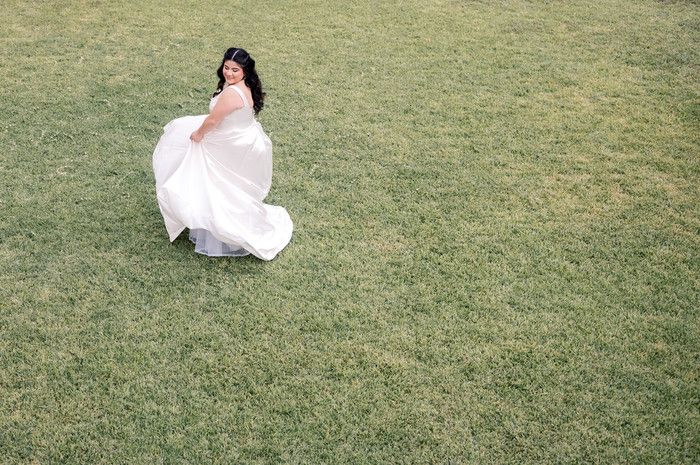 Beautiful bride spinning in elegant white wedding dress on lush green grass field.