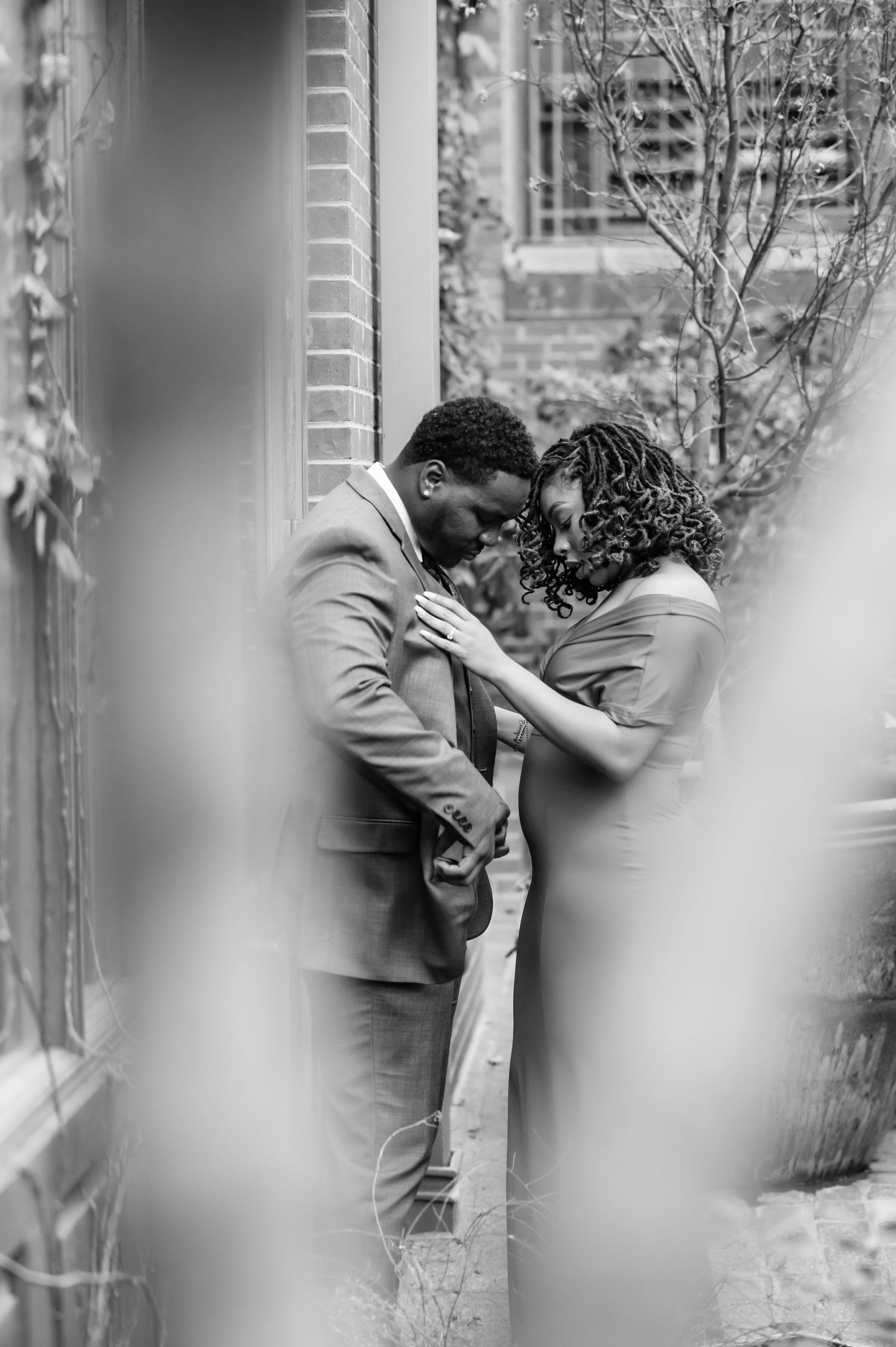 Black and white photo of couple sharing intimate moment, foreheads touching tenderly outdoors.
