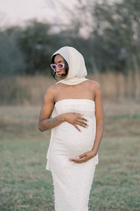 Artistic maternity photo with woman wrapped in white fabric against natural backdrop.