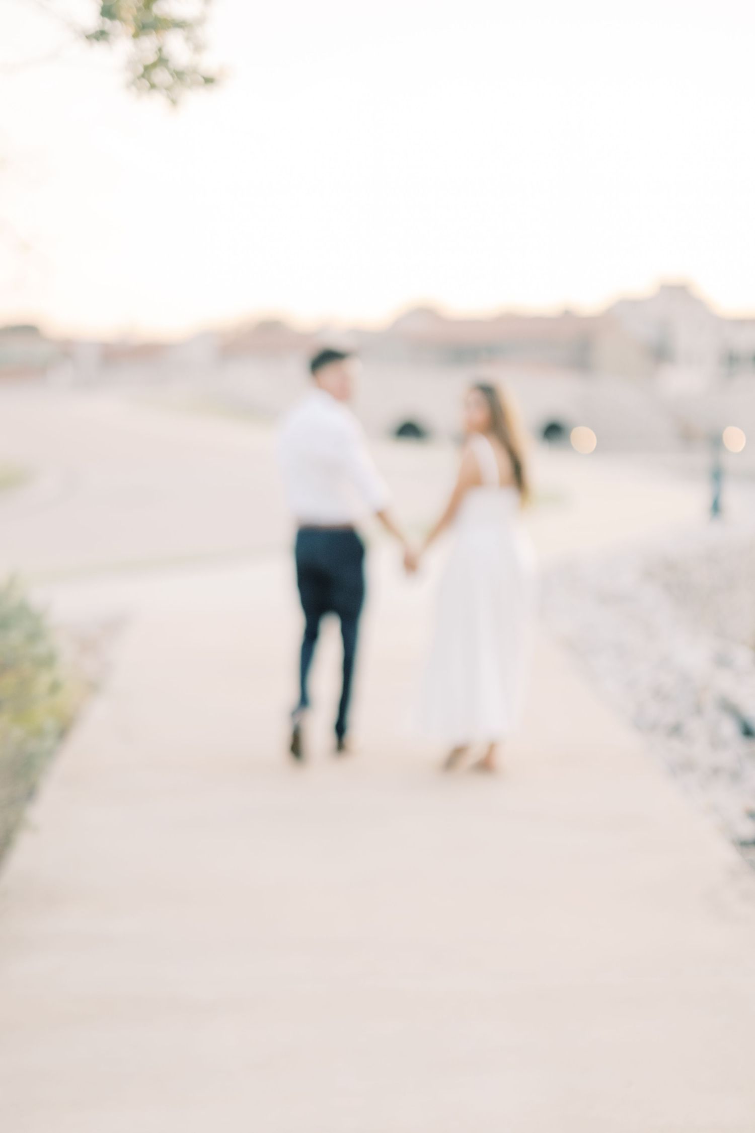 Blurred dreamy image of an engaged couple walking hand in hand along an outdoor path.