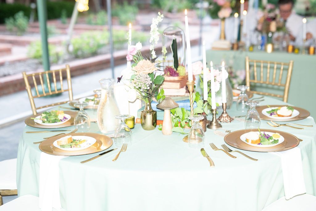 Elegant mint green wedding reception table with gold chargers, candles, floral centerpiece, and Chiavari chairs outdoors.