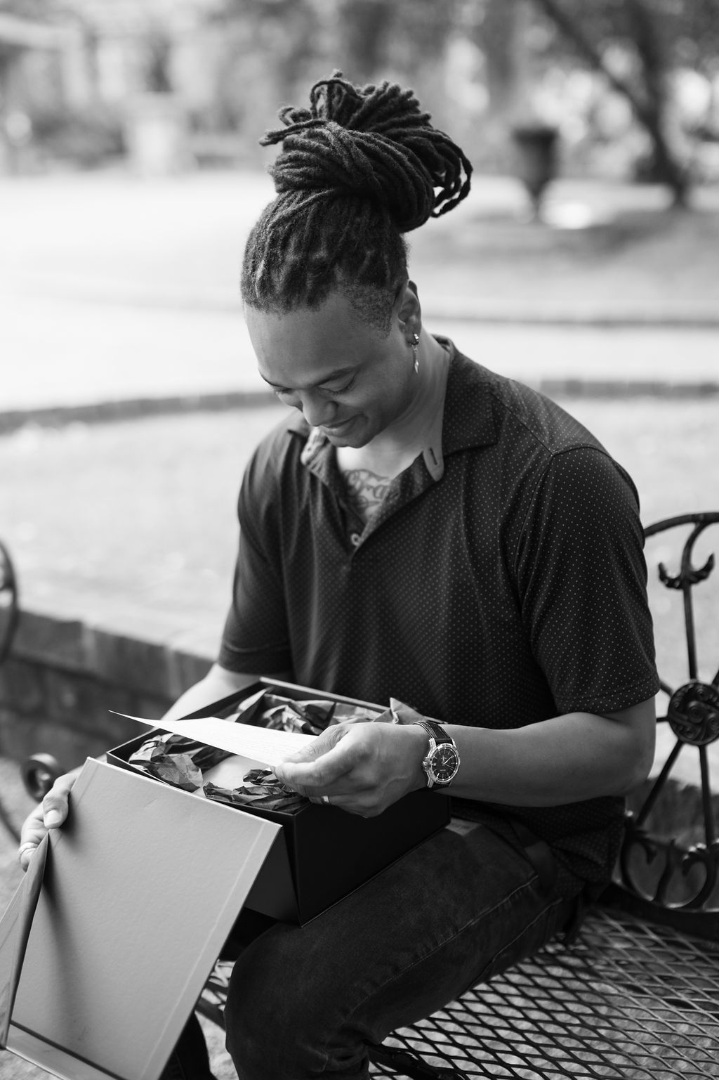 Black and white photo of a man with dreadlocks sitting on a bench, smiling while looking at photos in a box.