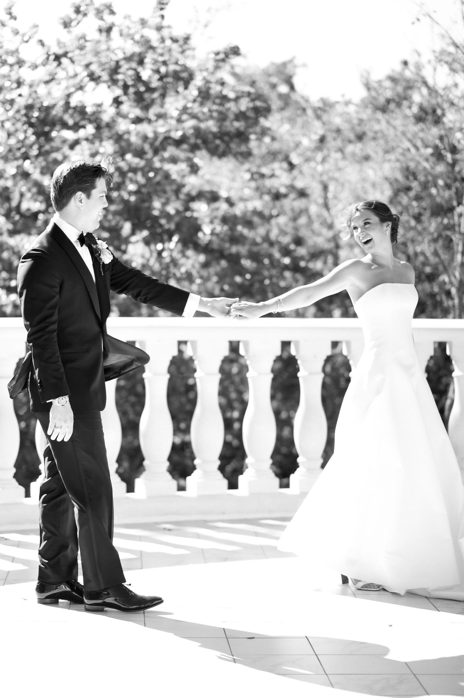 A black and white photo of a couple dancing on an elegant terrace with ornate stone railings.