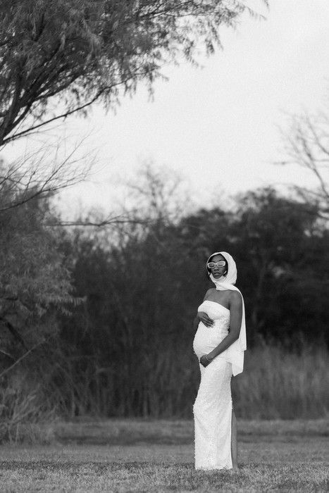Elegant white gown stands out against a natural backdrop of trees and grass in black and white photography.