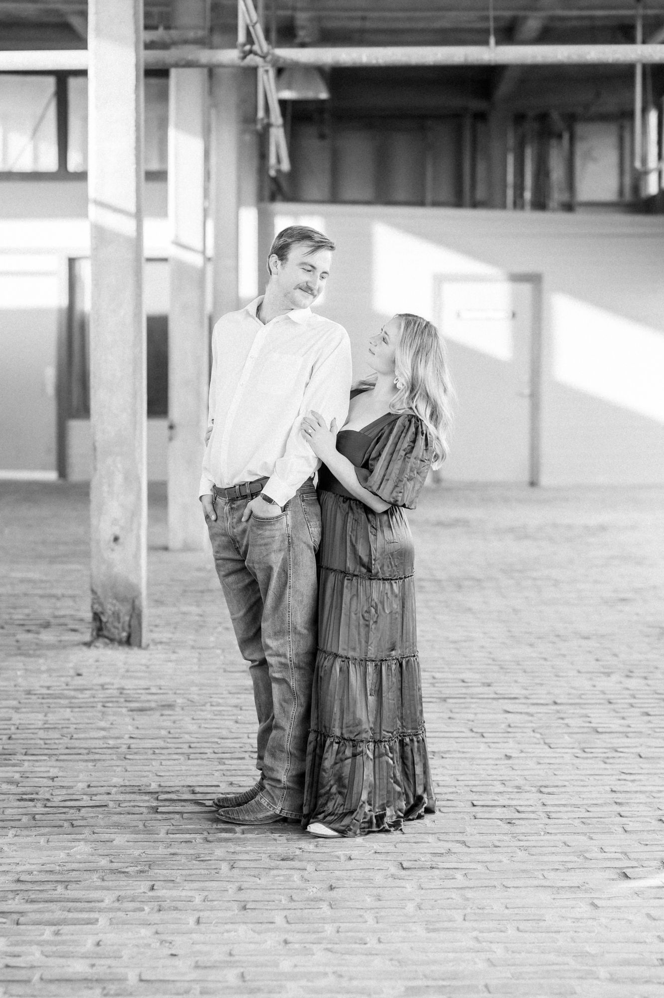 A romantic black and white portrait of a couple sharing a tender moment in an industrial indoor setting with brick floors.