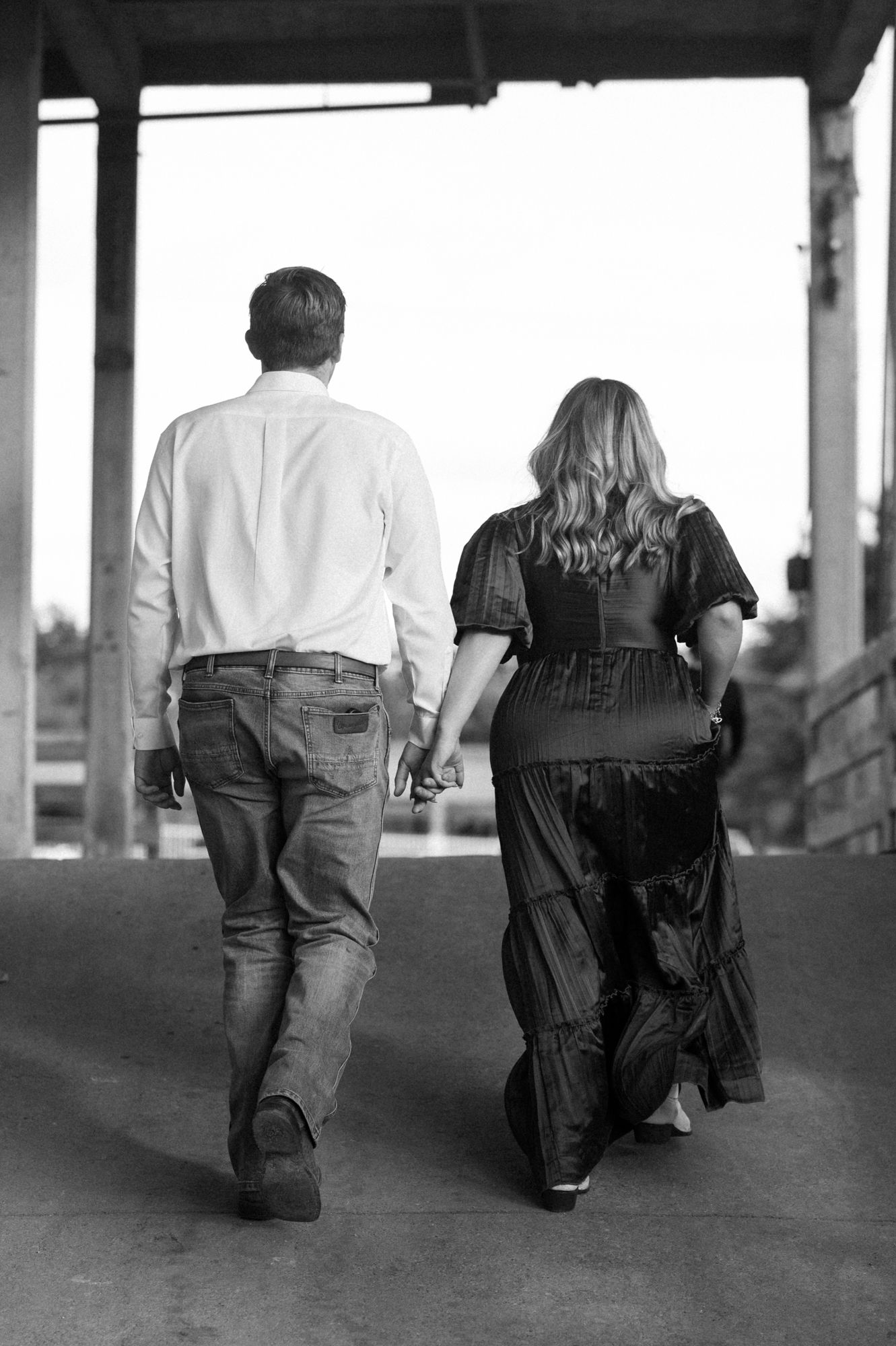 A black and white photo of a couple walking hand in hand down a covered walkway.