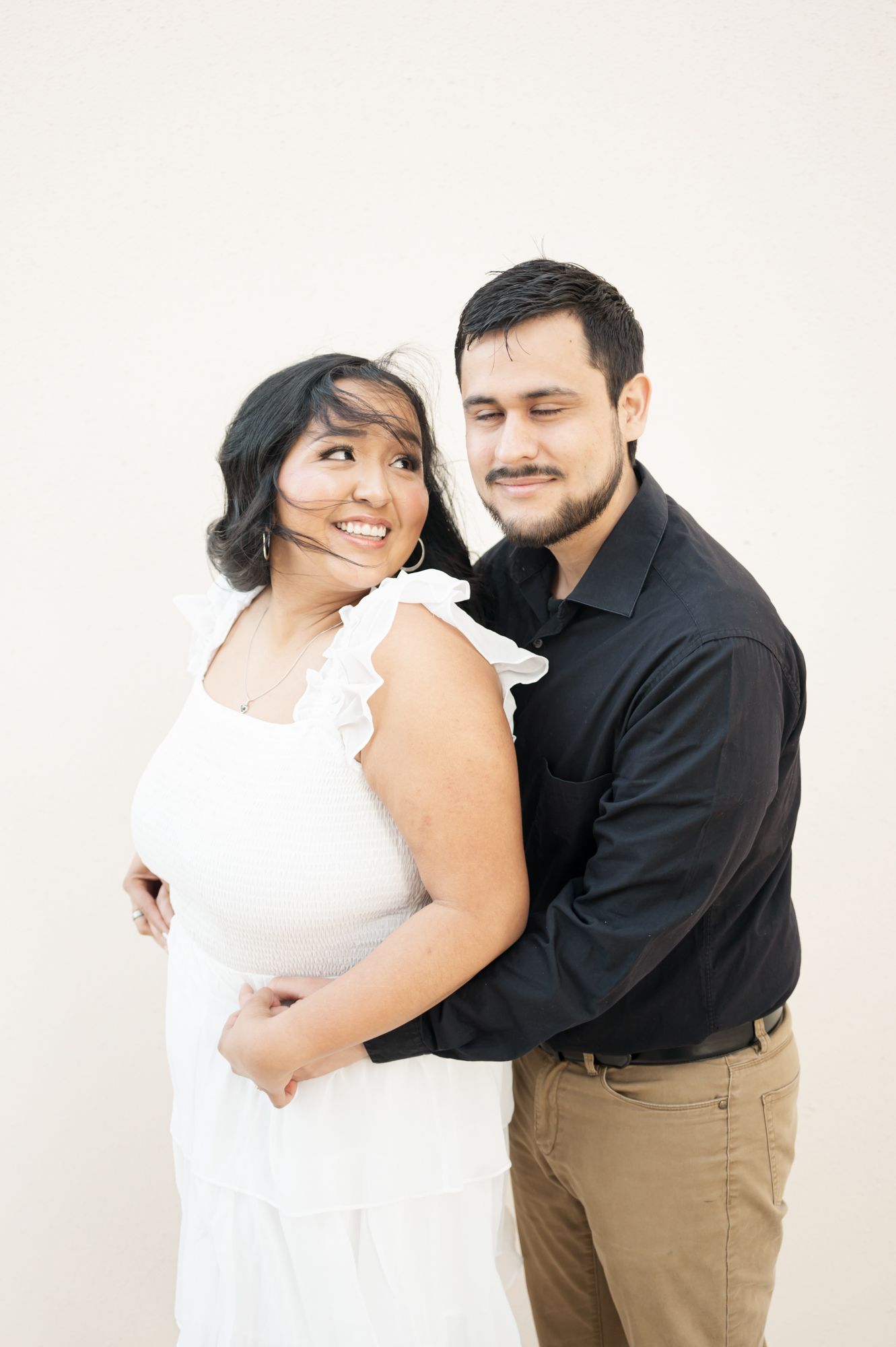 A couple in contrasting black and white outfits poses against a cream-colored wall.