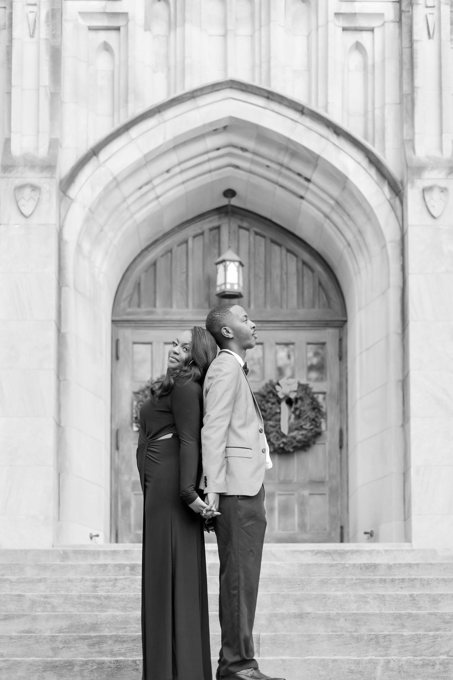 Black and white photo of a couple holding hands and looking up in front of a grand arched entrance.