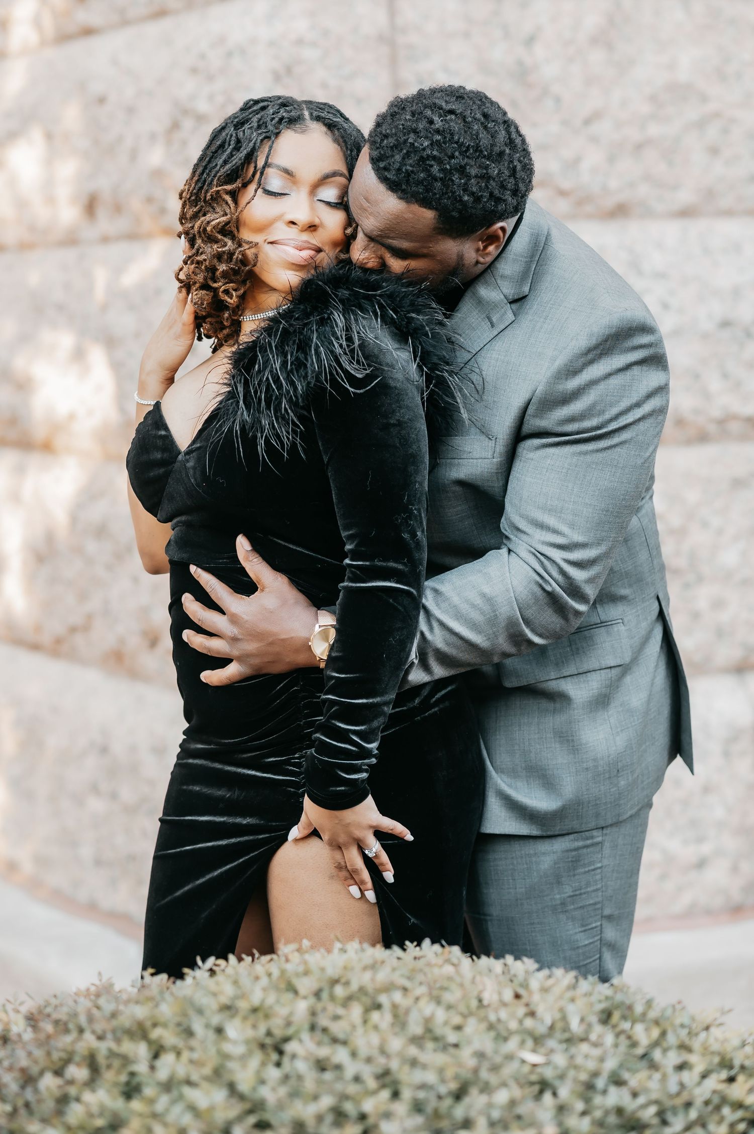 Couple in elegant black velvet dress and gray suit embracing romantically outdoors.