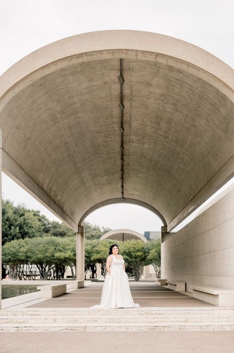 Bride in white gown under large concrete tunnel archway outdoors.