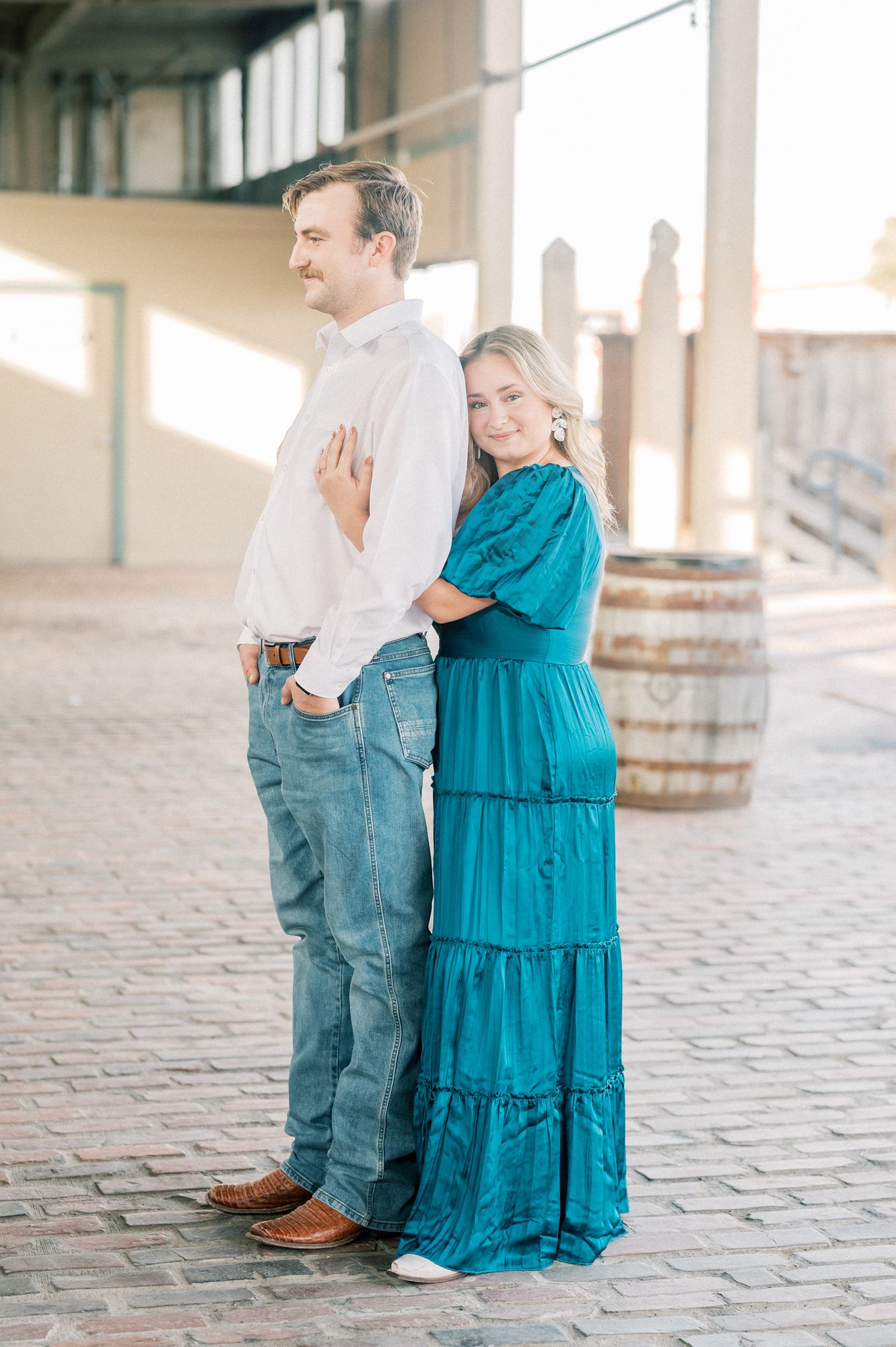 Couple in coordinated white and turquoise outfits pose playfully on brick floor.