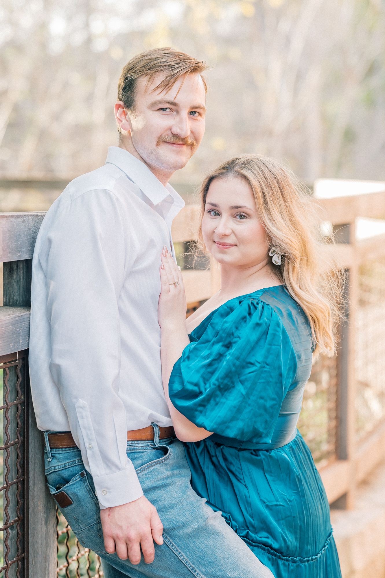 A couple in casual attire share a romantic moment on a wooden deck during a sunny outdoor photoshoot.