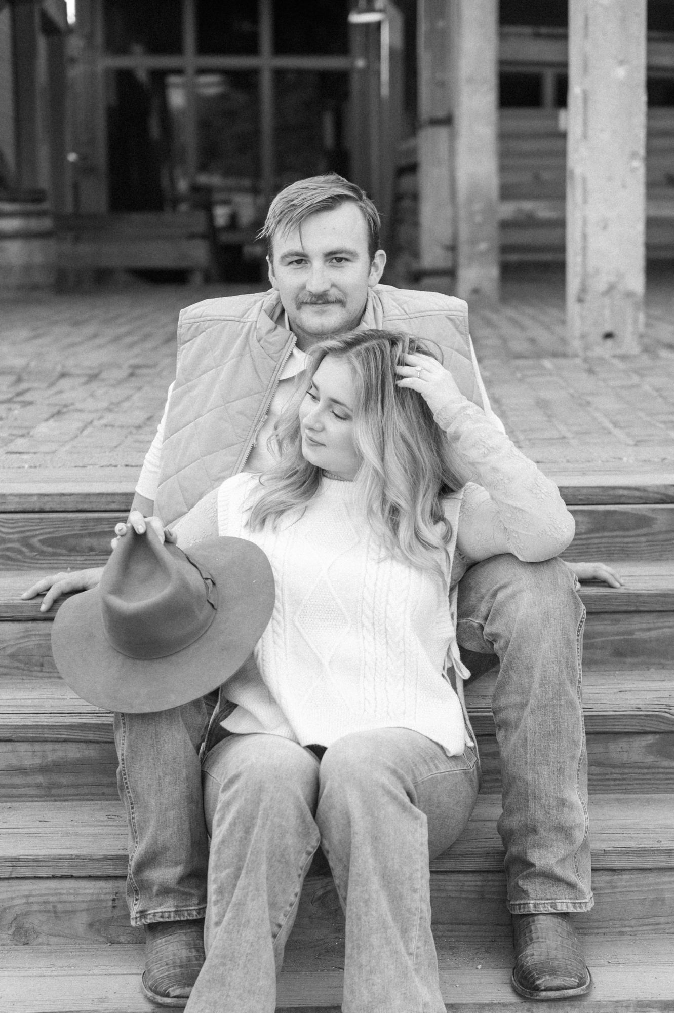 A couple sitting on wooden steps in casual attire sharing an intimate moment.