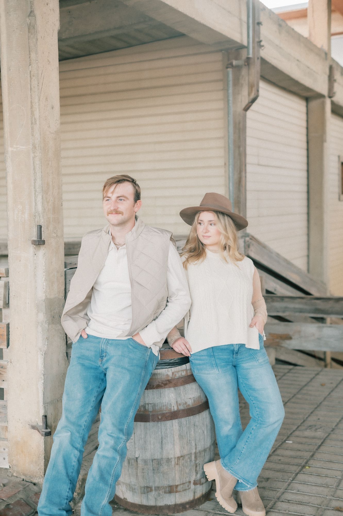 Couple in matching denim and light tops posing against a rustic wooden barrel.