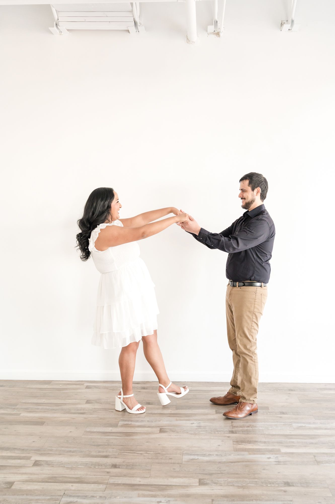 Playful couple dancing and twirling together in a bright white studio space.