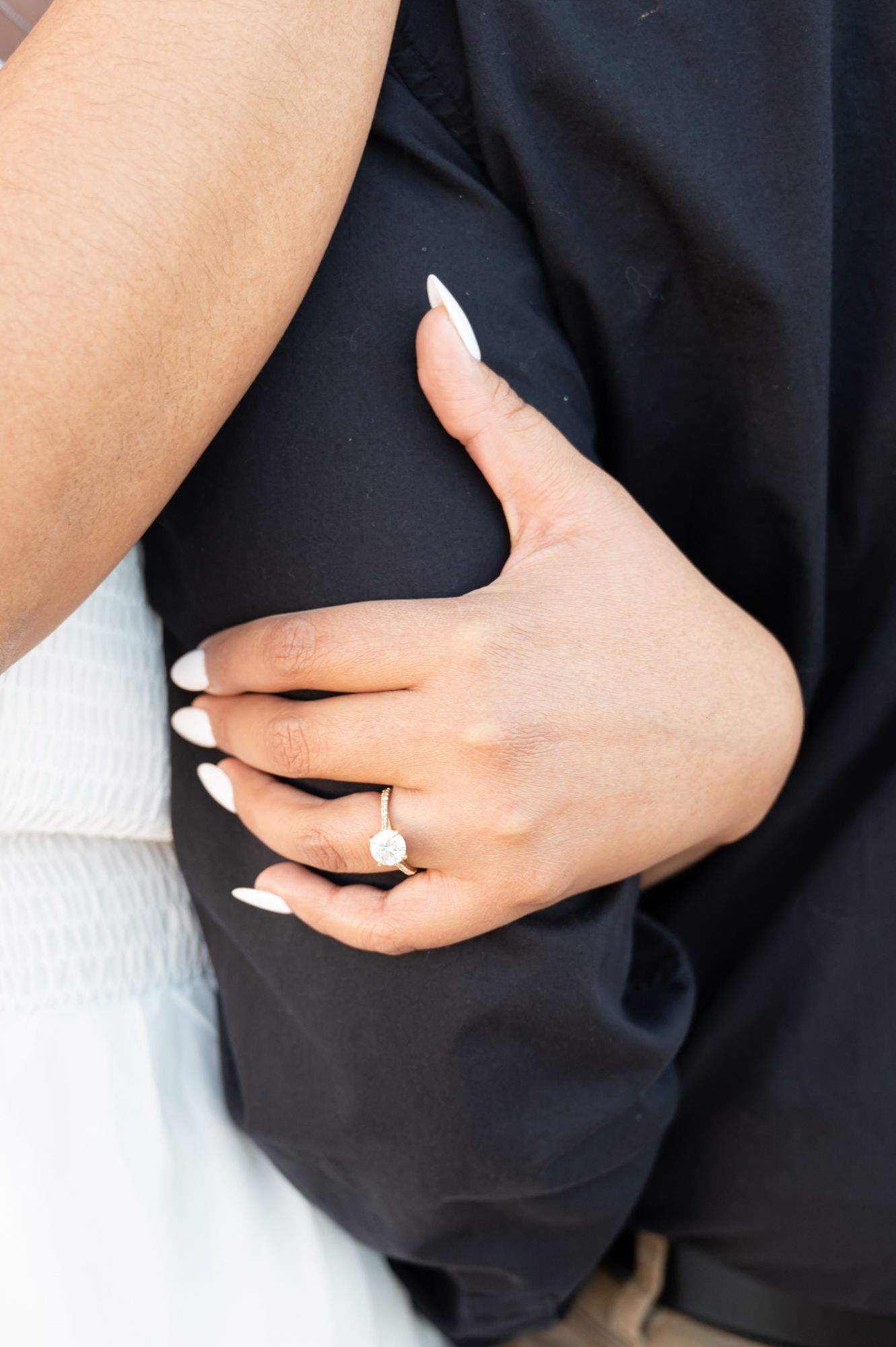 Close-up of hands embracing with an engagement ring visible against black and white clothing.