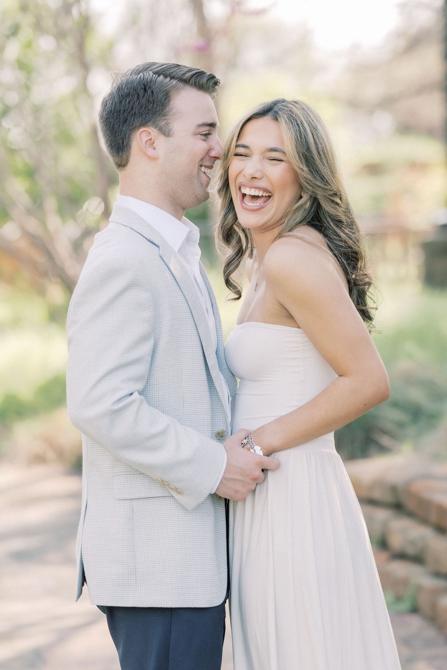 A couple in wedding attire share joyful moments and laughter during an outdoor photo session in natural lighting.