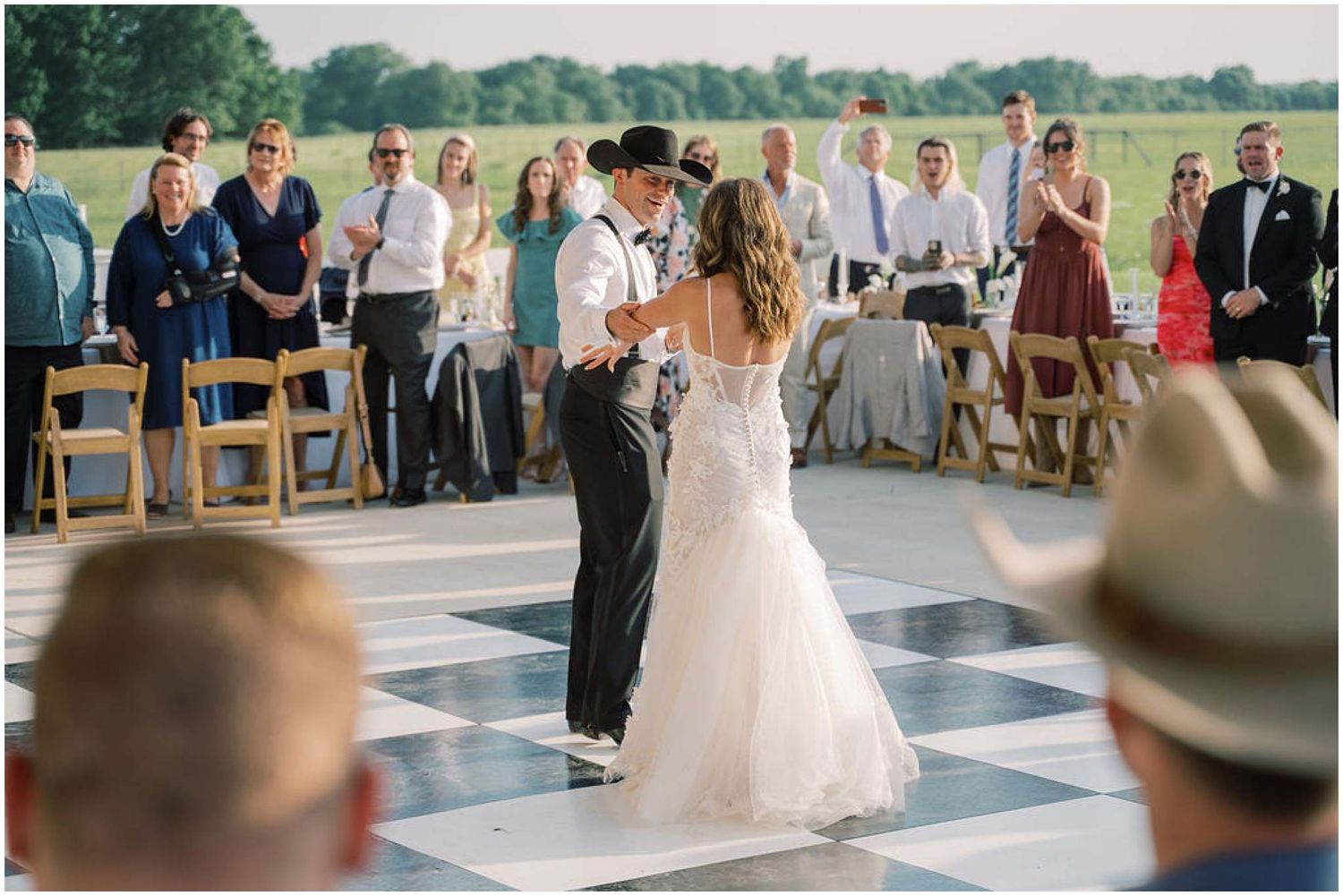 Couple sharing their first dance on checkered dance floor surrounded by wedding guests.