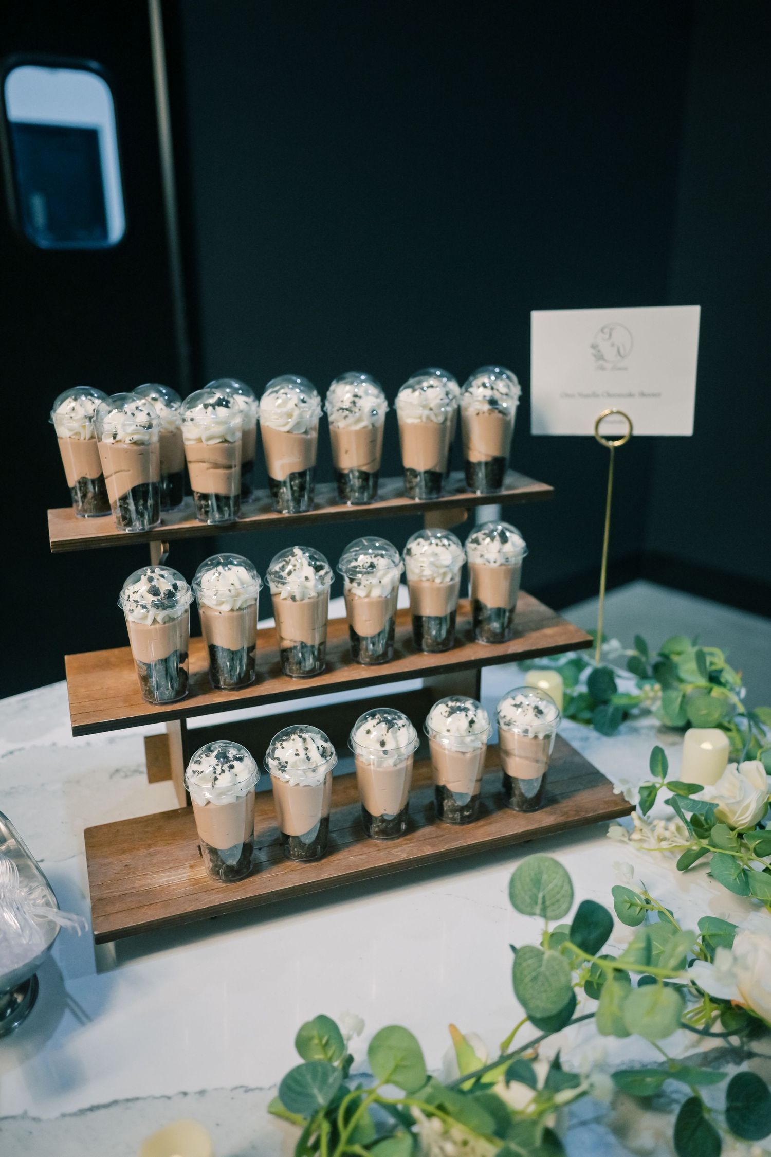 Three-tiered wooden display of chocolate mousse push-up dessert cups topped with whipped cream at a wedding reception.